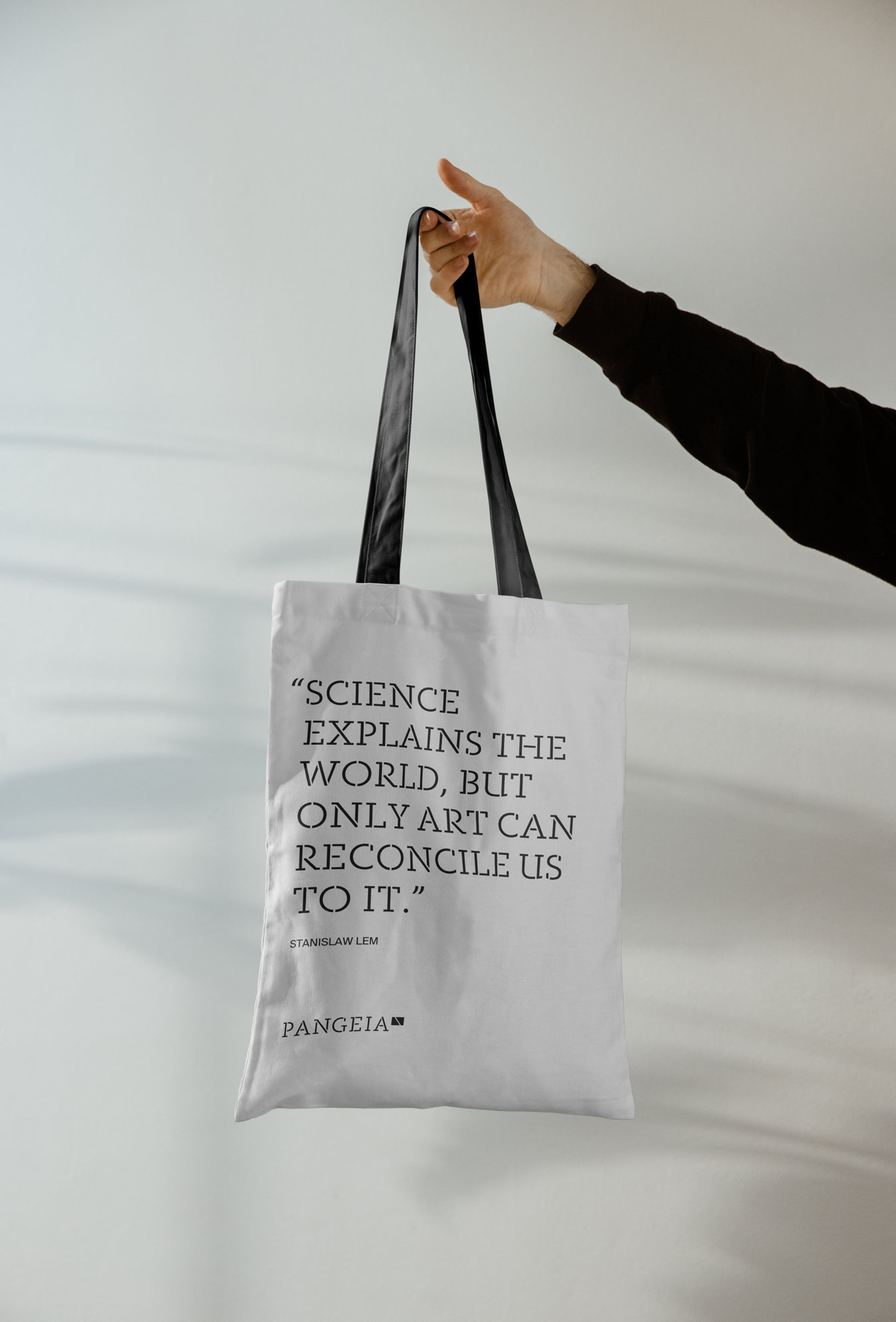 Hand holding a totebag with PANGEIA branding and the phrase "Science explains the world, but only art can reconcile us." from Stanislaw Lem.